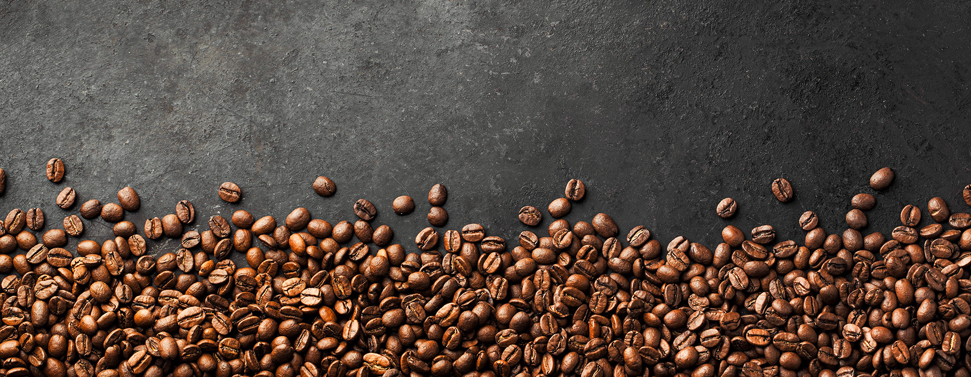 Kaffeebohnen als stimmungsvoller Hintergrund fuer warme Getraenke bei Caviani
